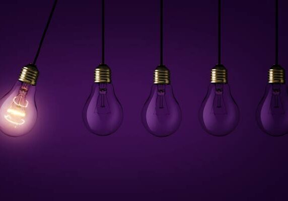 Five lightbulbs with one lit and purple dark background.